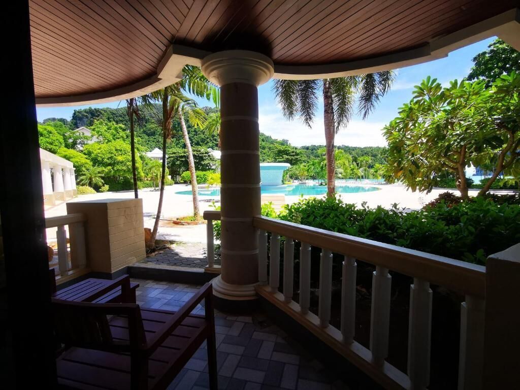 A covered outdoor area with a view of a pool and lush greenery.