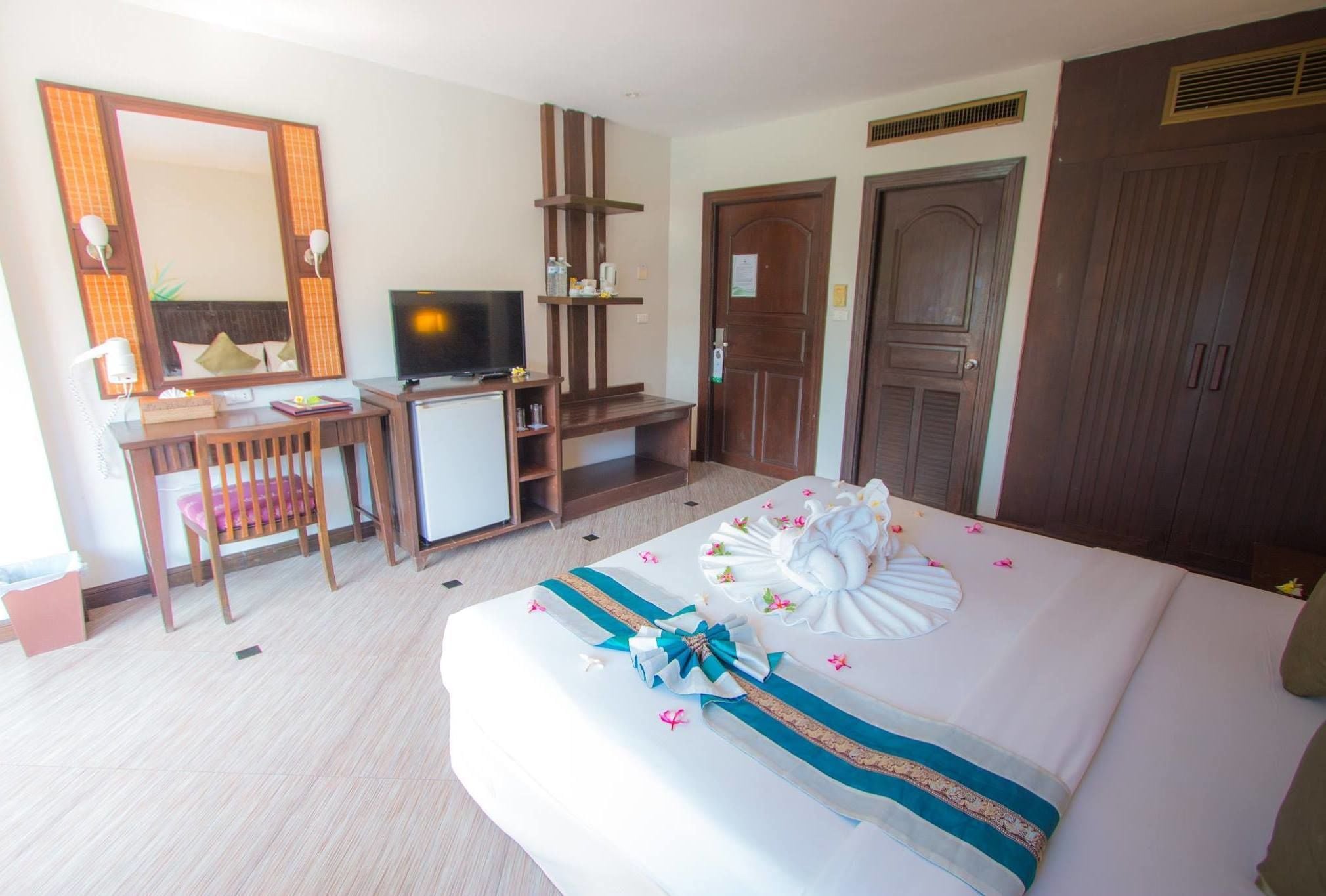 Una habitación de hotel con una cama, un escritorio con televisor, un armario y un espejo.