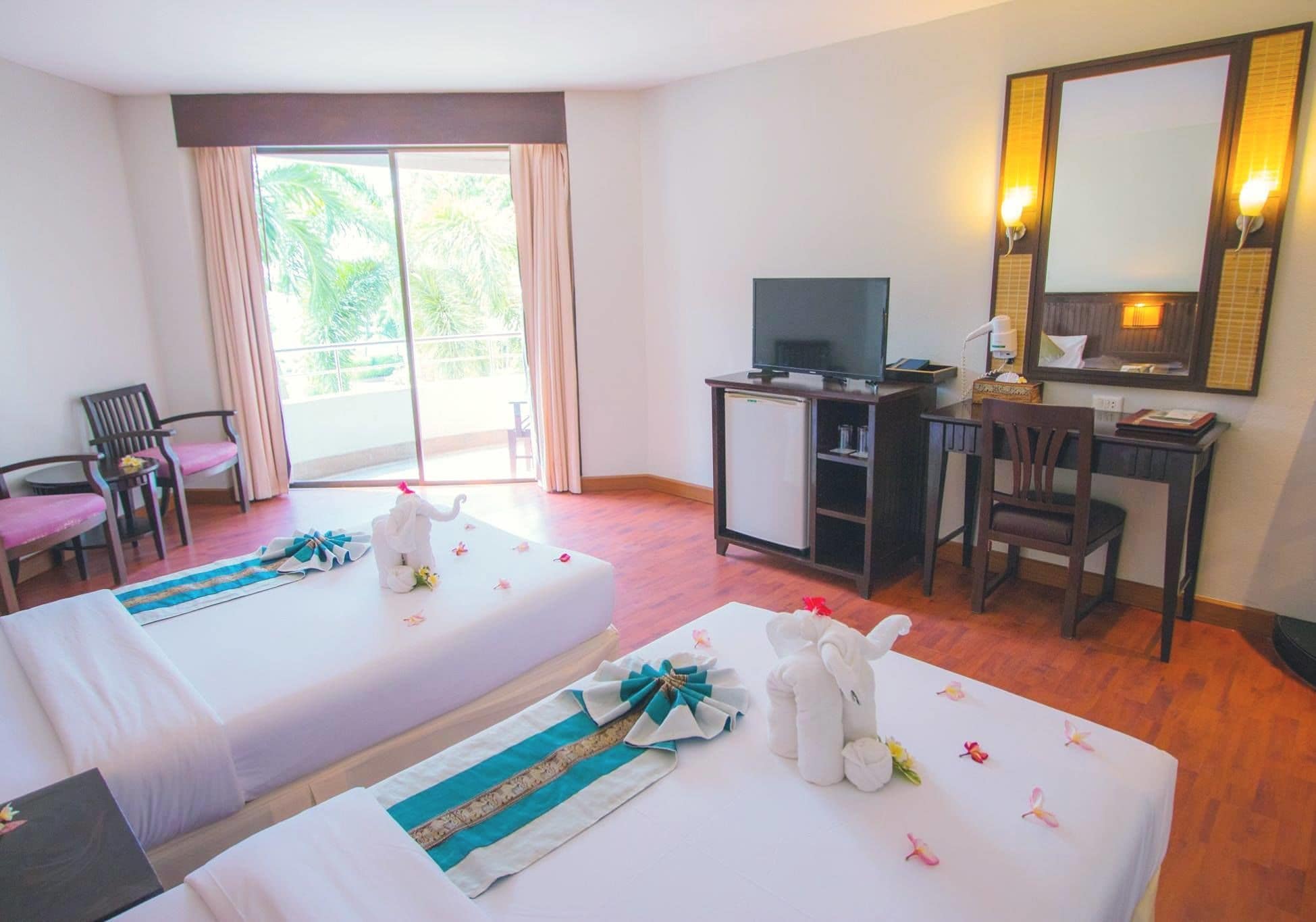 A hotel room with two beds, a desk, a television, and a large window with curtains.