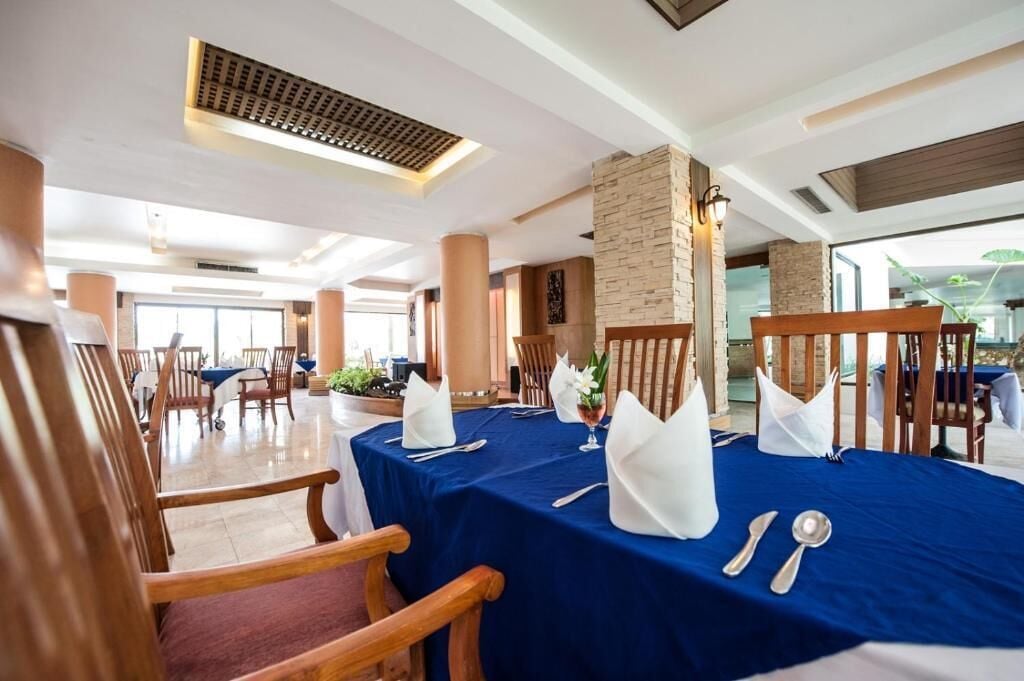Comedor con mesas dispuestas para cuatro, con manteles azules, servilletas blancas y cubiertos.