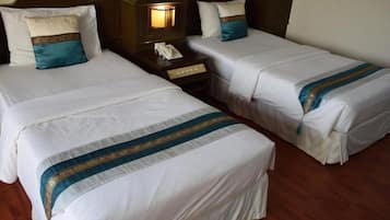 Two single beds with white linens and teal accents, a nightstand with a telephone, and a wooden headboard.