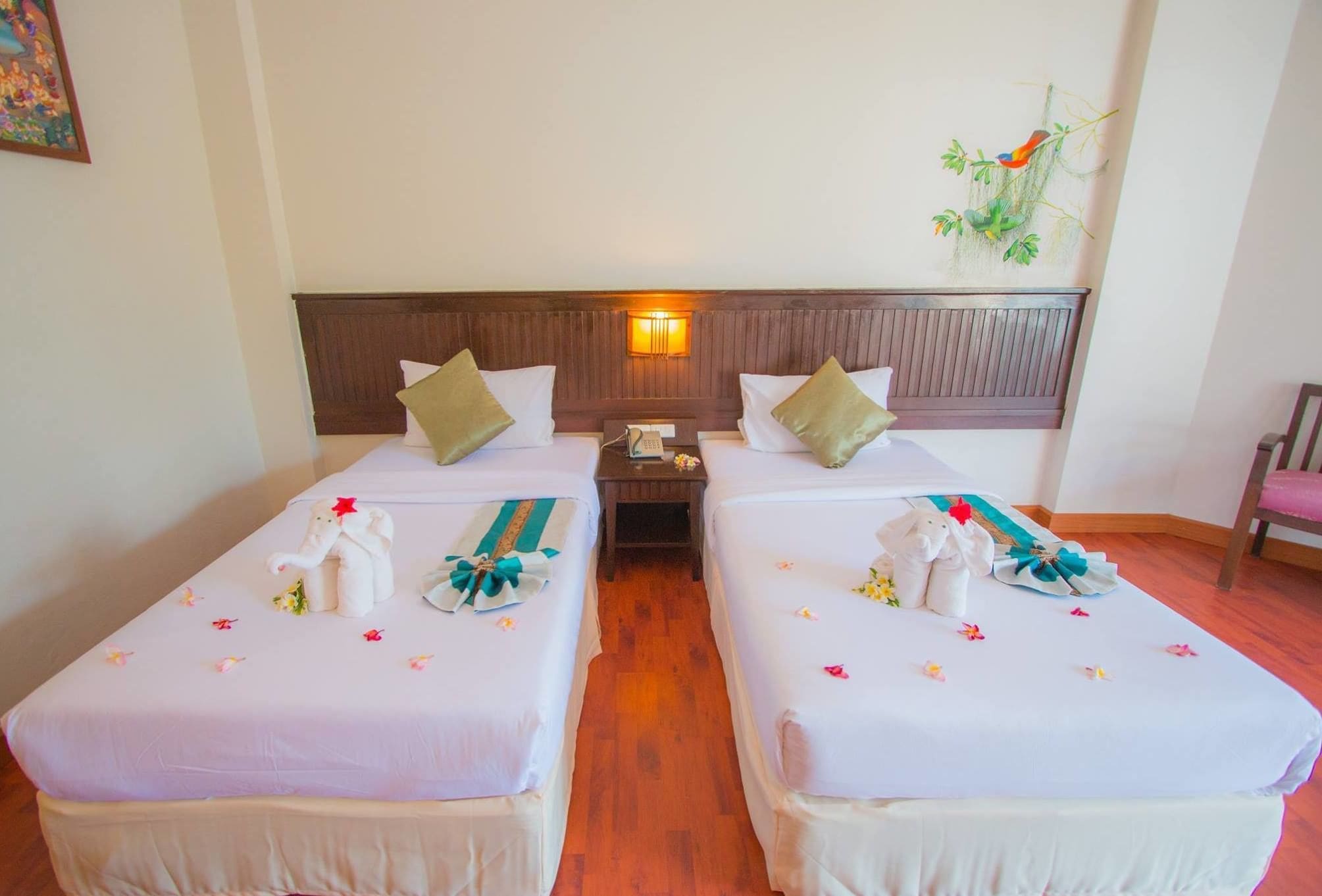 A hotel room with two single beds, a wooden headboard, a nightstand with a lamp, and a wall-mounted plant.