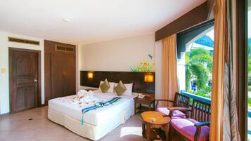 Habitación de hotel con una cama grande, una mesita, dos sillas, una mesita de noche y una ventana con cortinas.