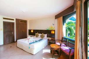 Habitación de hotel con una cama grande, una mesita, dos sillas, una mesita de noche y una ventana con cortinas.