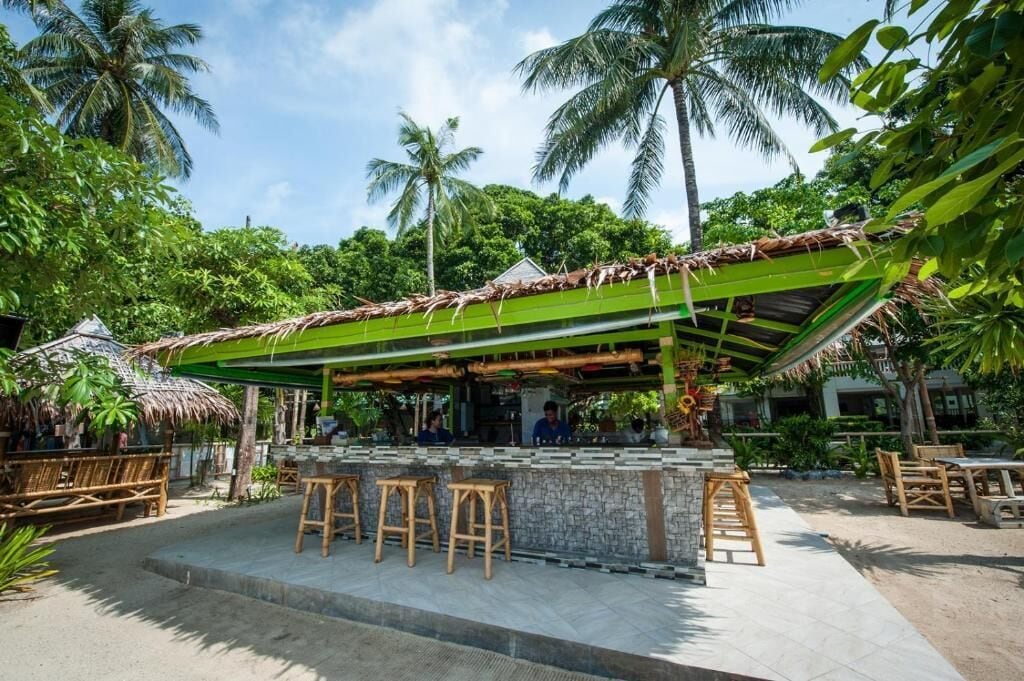An outdoor bar area with a green roof, stone counter, and wooden stools.