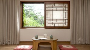 A room with a wooden table, two cushions, a window with a view of greenery, and a traditional screen door. - Onyang Hot Spring Hotel (Asan)