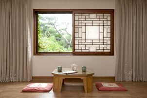 Una habitación con una mesa de madera, dos cojines, un ventanal con vistas a la vegetación y una puerta corrediza tradicional.