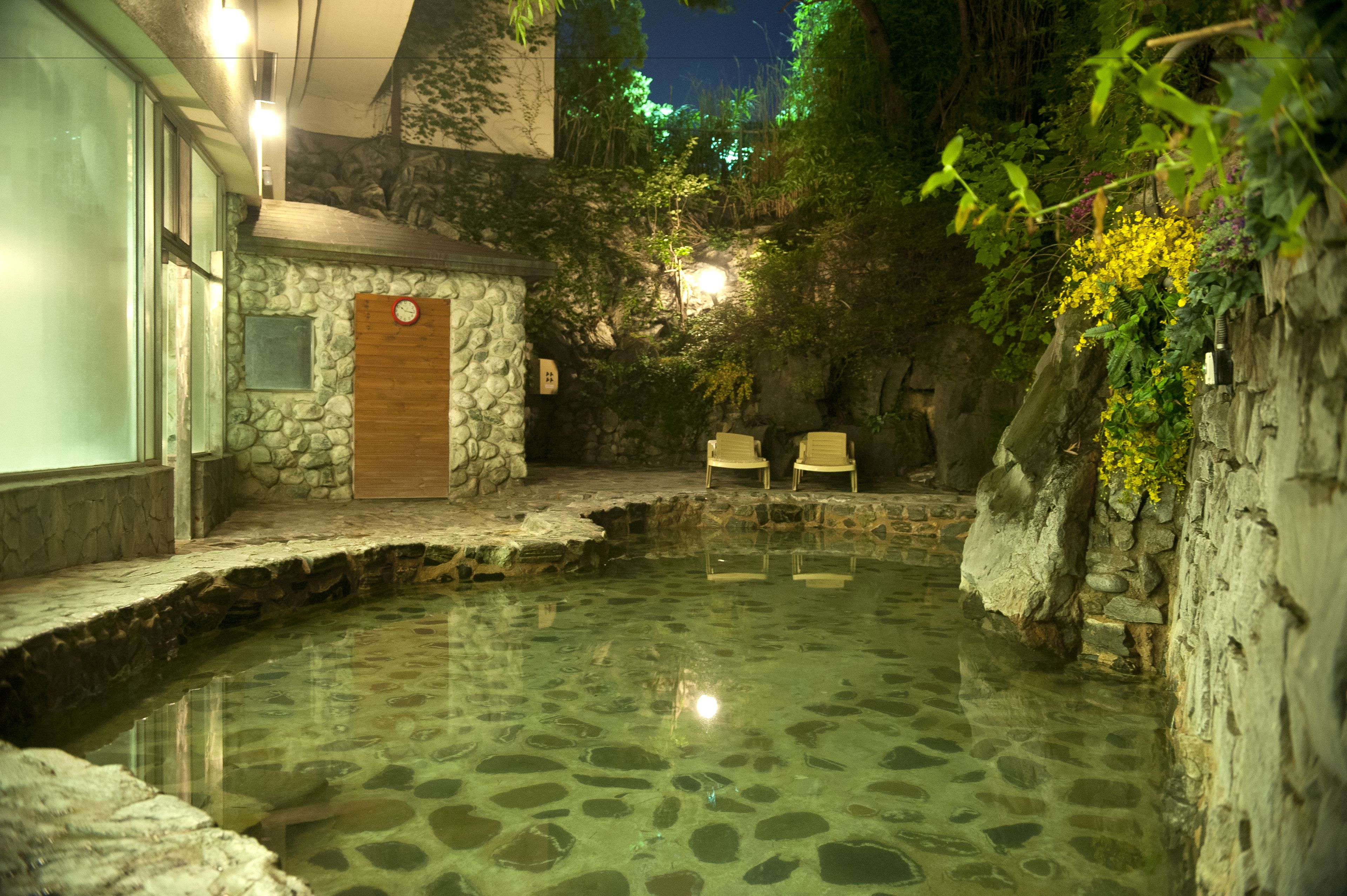 Zona de aguas termales con paredes de piedra, dos sillas y una puerta de madera.