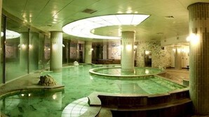 A large indoor swimming pool with multiple circular sections, surrounded by columns and walls with patterned designs. - Onyang Hot Spring Hotel (Asan)