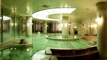 Una amplia piscina cubierta con varias secciones circulares, rodeada de columnas y paredes con diseños decorativos.
