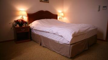 Habitación de hotel con una cama individual, dos lámparas de noche, una mesita de noche con un jarrón de flores y suelo cubierto de alfombra.