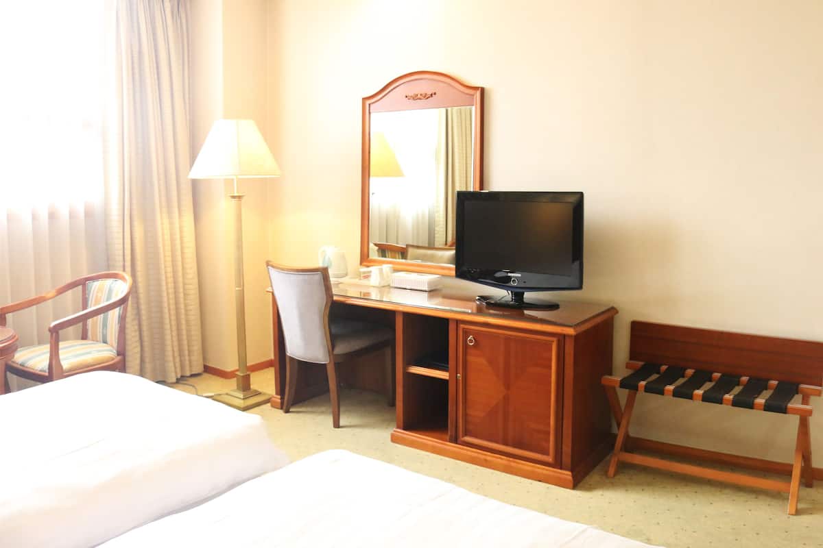 Una habitación de hotel con una cama, un escritorio con televisor, una silla, una lámpara y un banco.