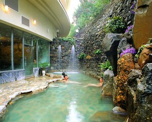 A spa area with a stone wall, a small waterfall, and a clear pool.