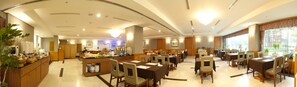 A hotel dining area with multiple tables and chairs, a buffet counter, and a view of the outdoors through large windows.