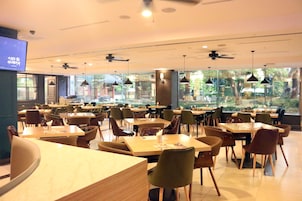 Un restaurante espacioso con numerosas mesas y sillas, grandes ventanales que ofrecen vistas al exterior, ventiladores de techo e iluminación colgante.