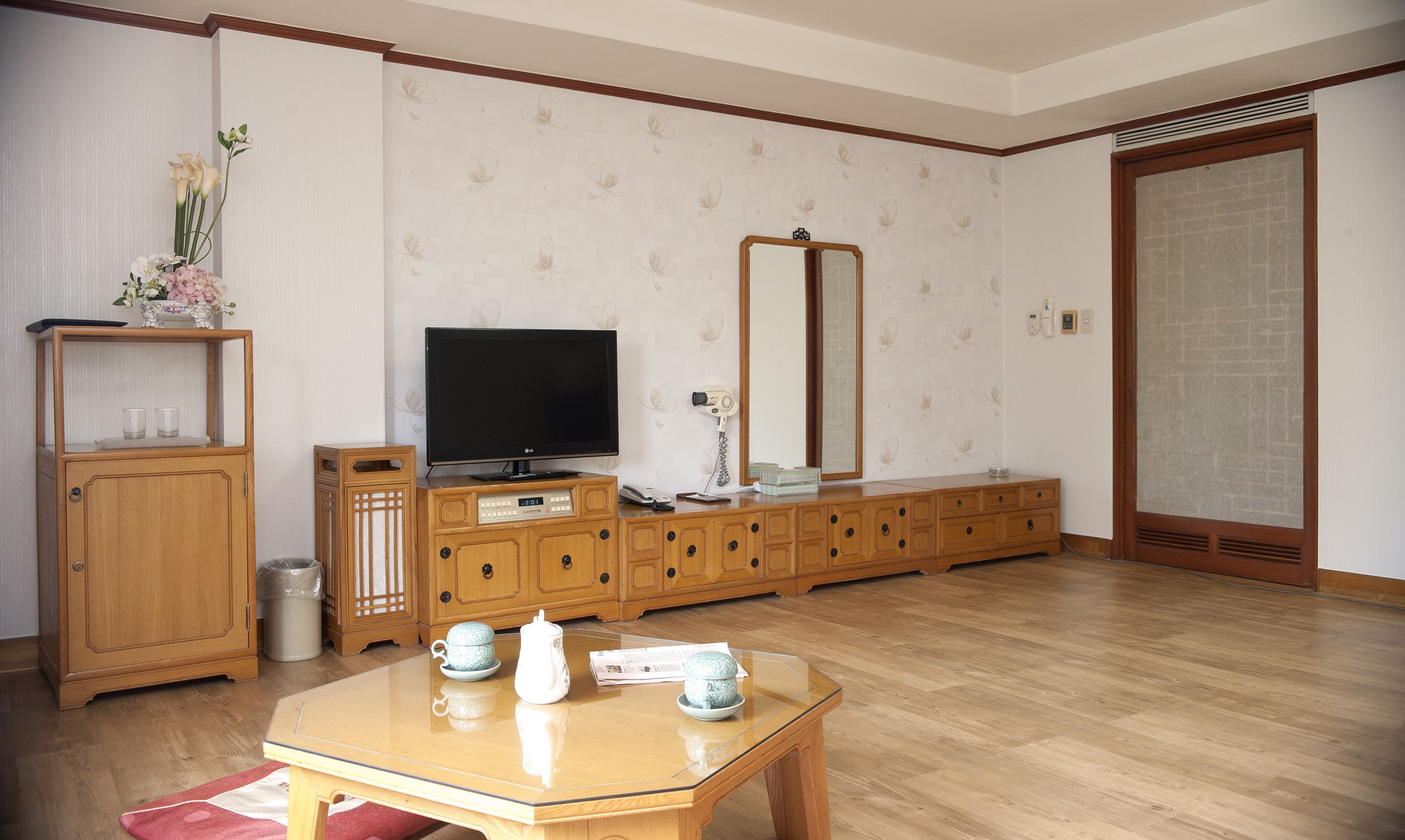 Una sala de estar con un mueble de madera, un televisor, un espejo y una mesa con tazas y papeles.