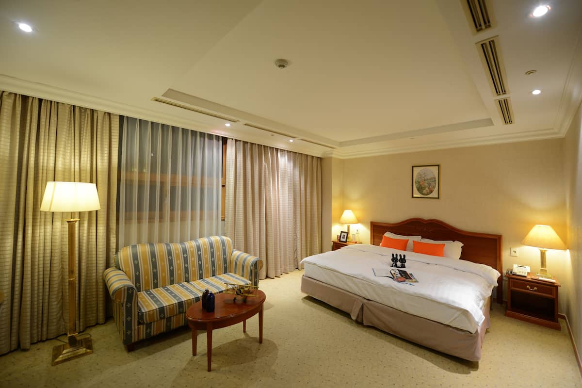 Una habitación de hotel con una cama grande, un sofá, una mesita y dos lámparas de noche.