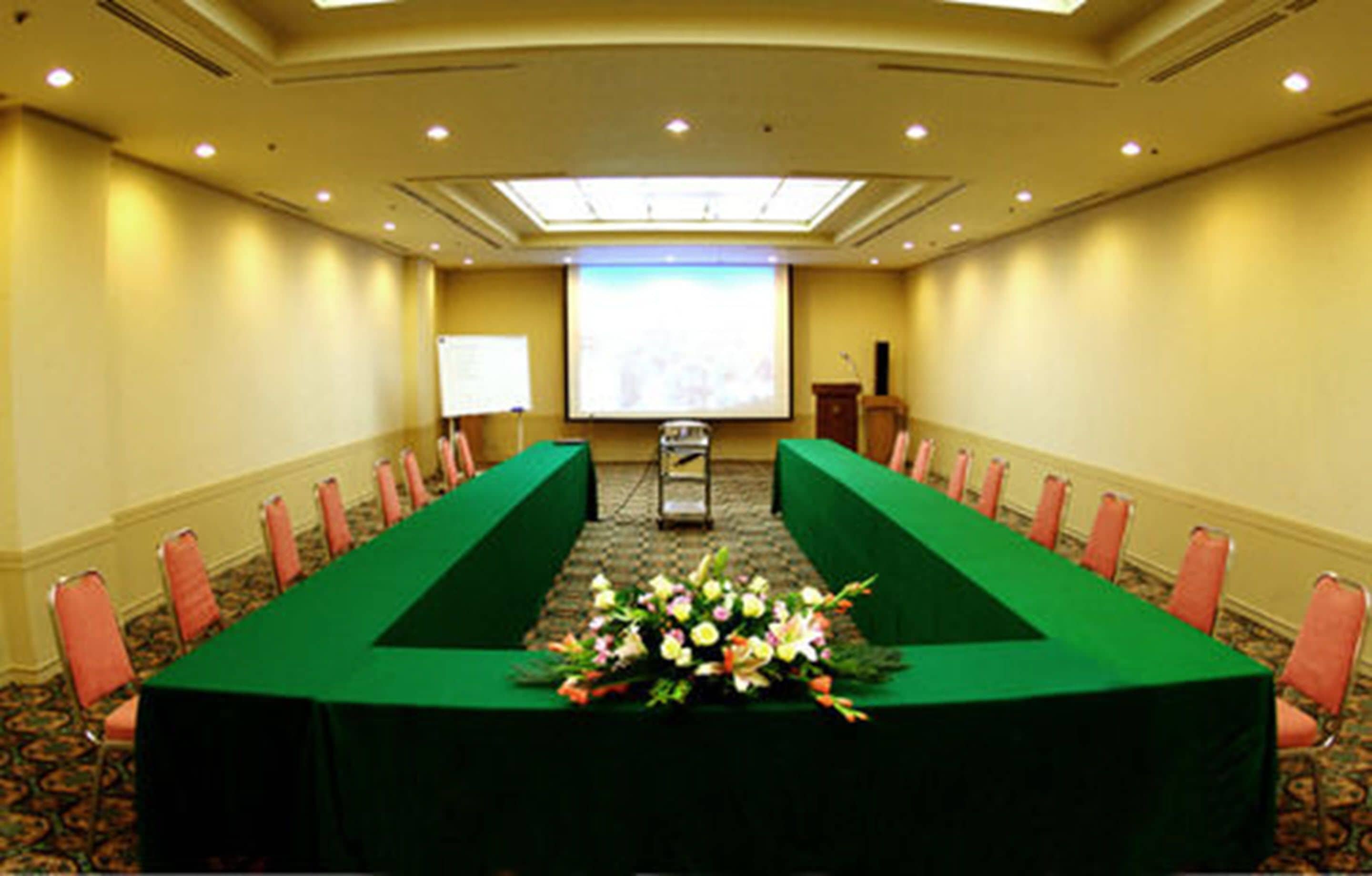 Une salle de conférence équipée d’une longue table, de chaises, d’un écran de projection et d’un pupitre.