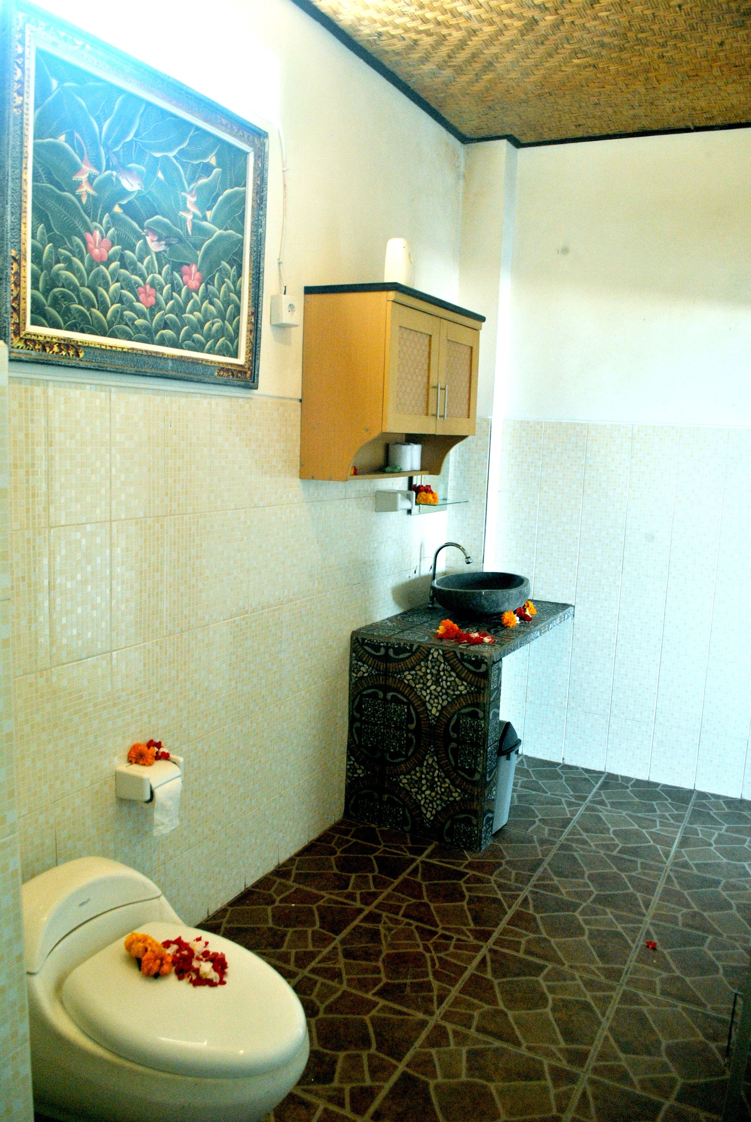 Une salle de bain comprenant des toilettes, un lavabo avec un récipient décoratif, un carrelage à motifs et une étagère murale sur laquelle est posé un rouleau de papier toilette.