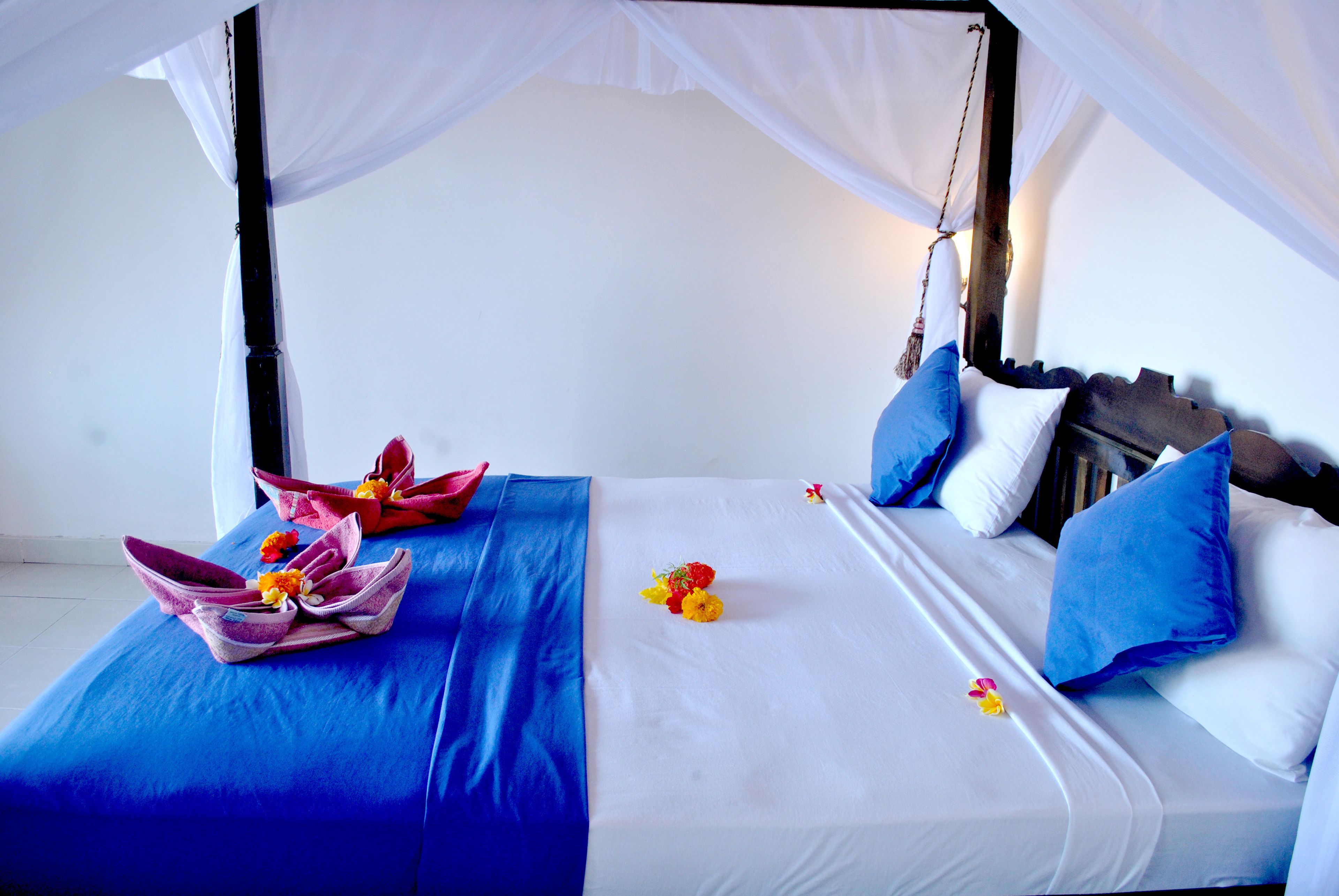 A bed with a canopy, blue bedding, and a floral arrangement.