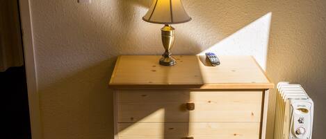 A room with a wooden nightstand, a lamp, a remote control, and a television mounted on the wall.