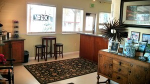A well-lit room with a wooden bar area, two stools, a large rug, and a cabinet with various items. - Green Gables Motel & Suites (Burney)