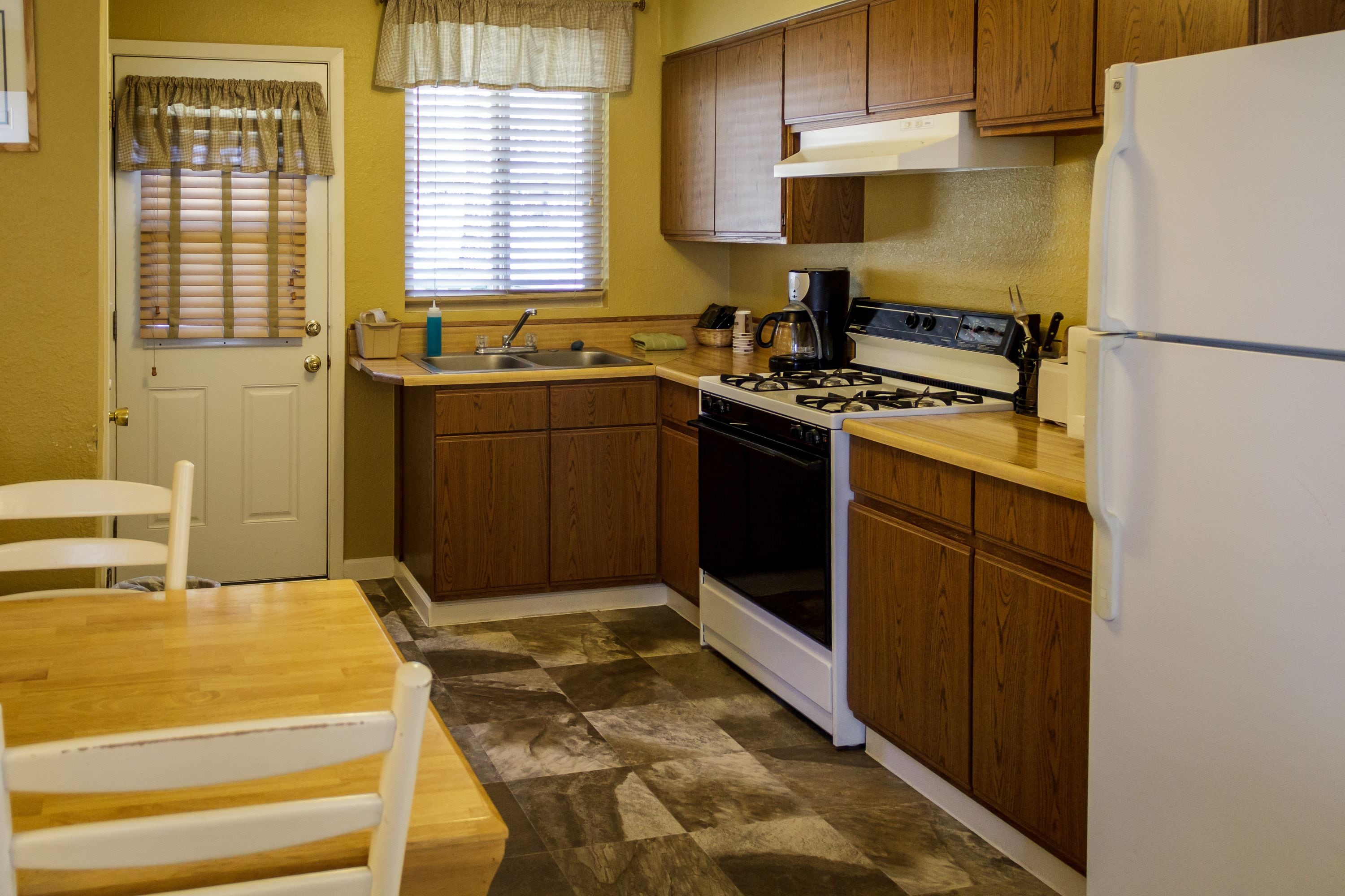 A compact kitchen with wooden cabinets, a white refrigerator, a stove, and a sink.