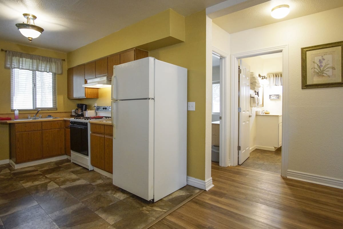 A kitchen with wooden cabinets, a white refrigerator, and a wooden floor.