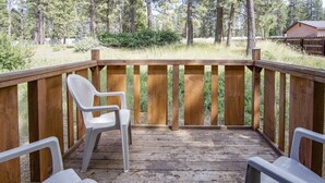 A wooden deck with two white plastic chairs and a wooden railing. - Green Gables Motel & Suites (Burney)