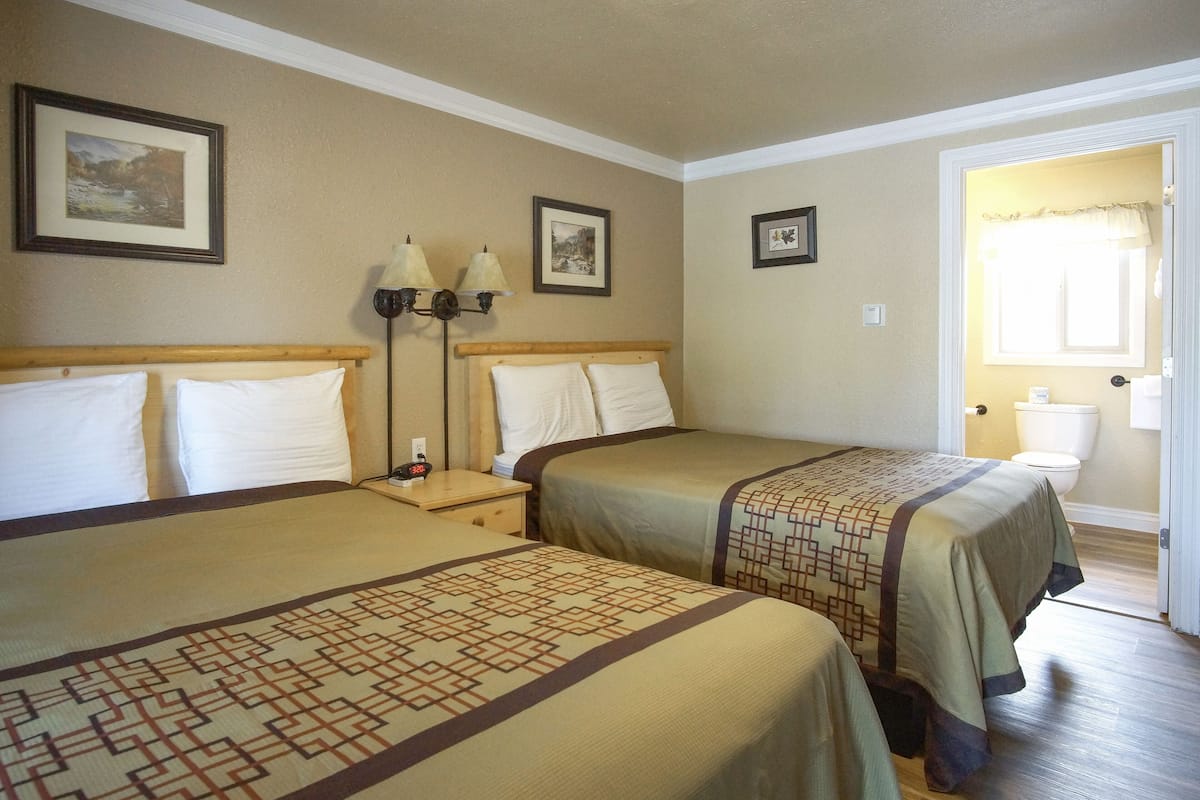 A hotel room with two beds, a nightstand with lamps, and a door leading to the bathroom.