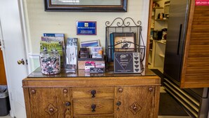 A wooden cabinet with drawers, a glass jar with flowers, and various items on top including books and a framed certificate. - Green Gables Motel & Suites (Burney)