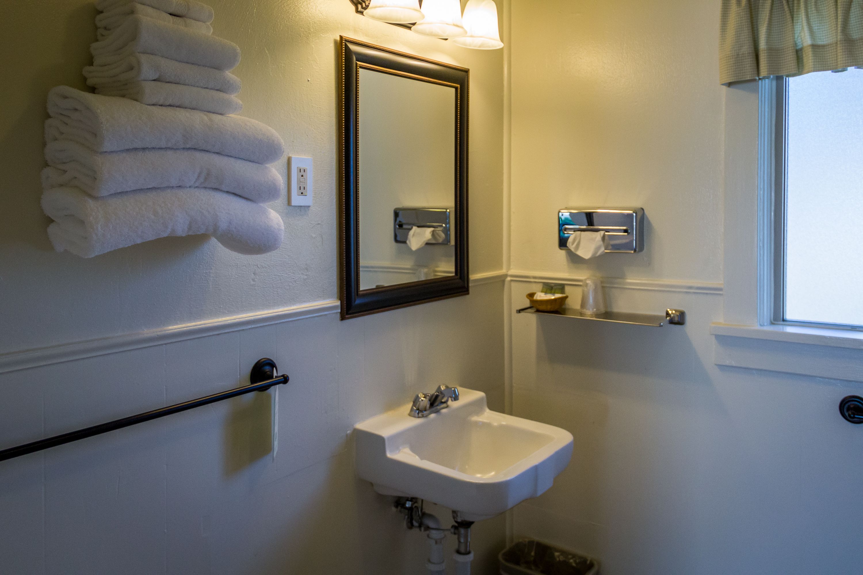 A bathroom with a sink, mirror, towel rack, and window.