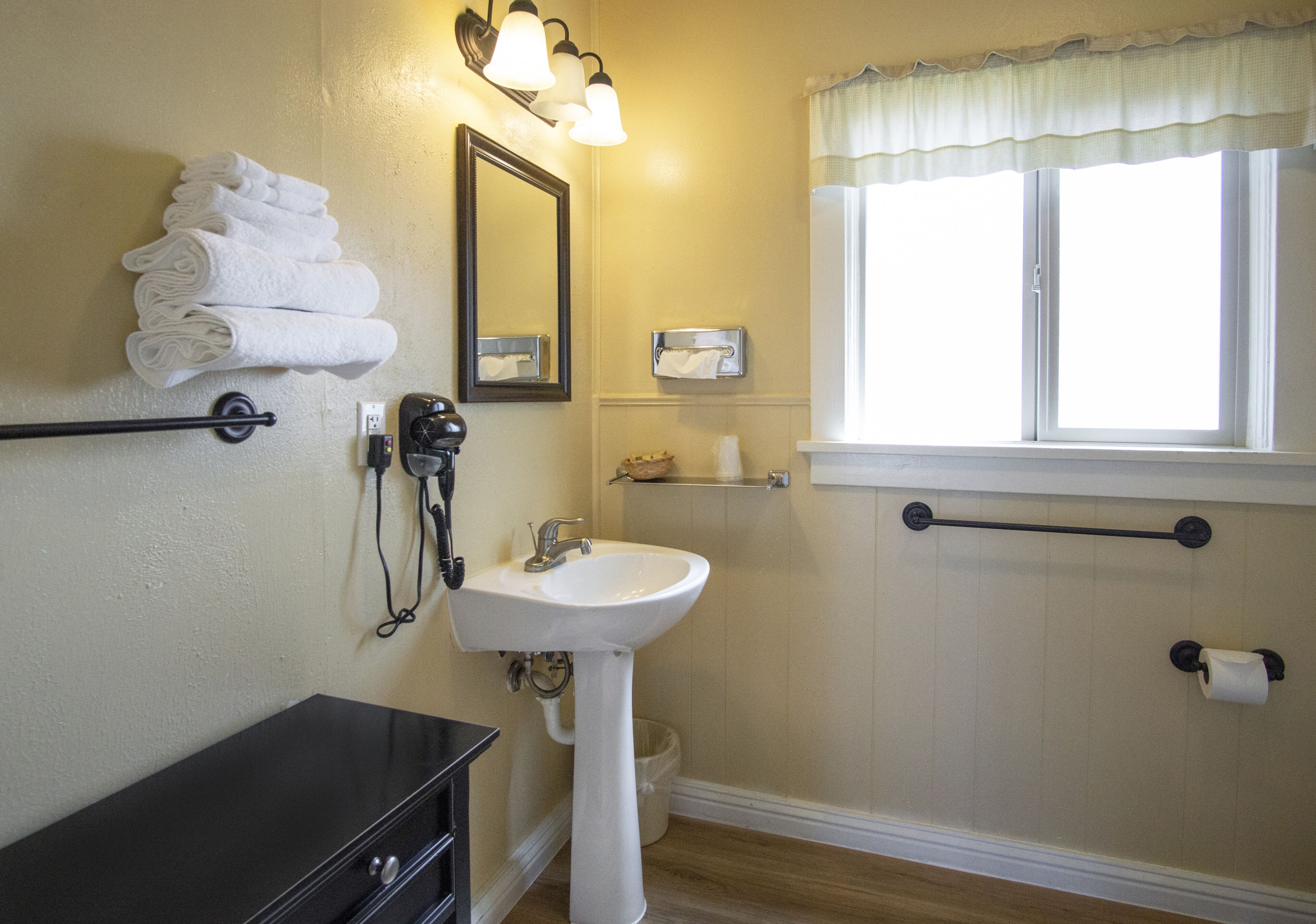 Un baño con lavamanos, espejo, toallero y ventana.