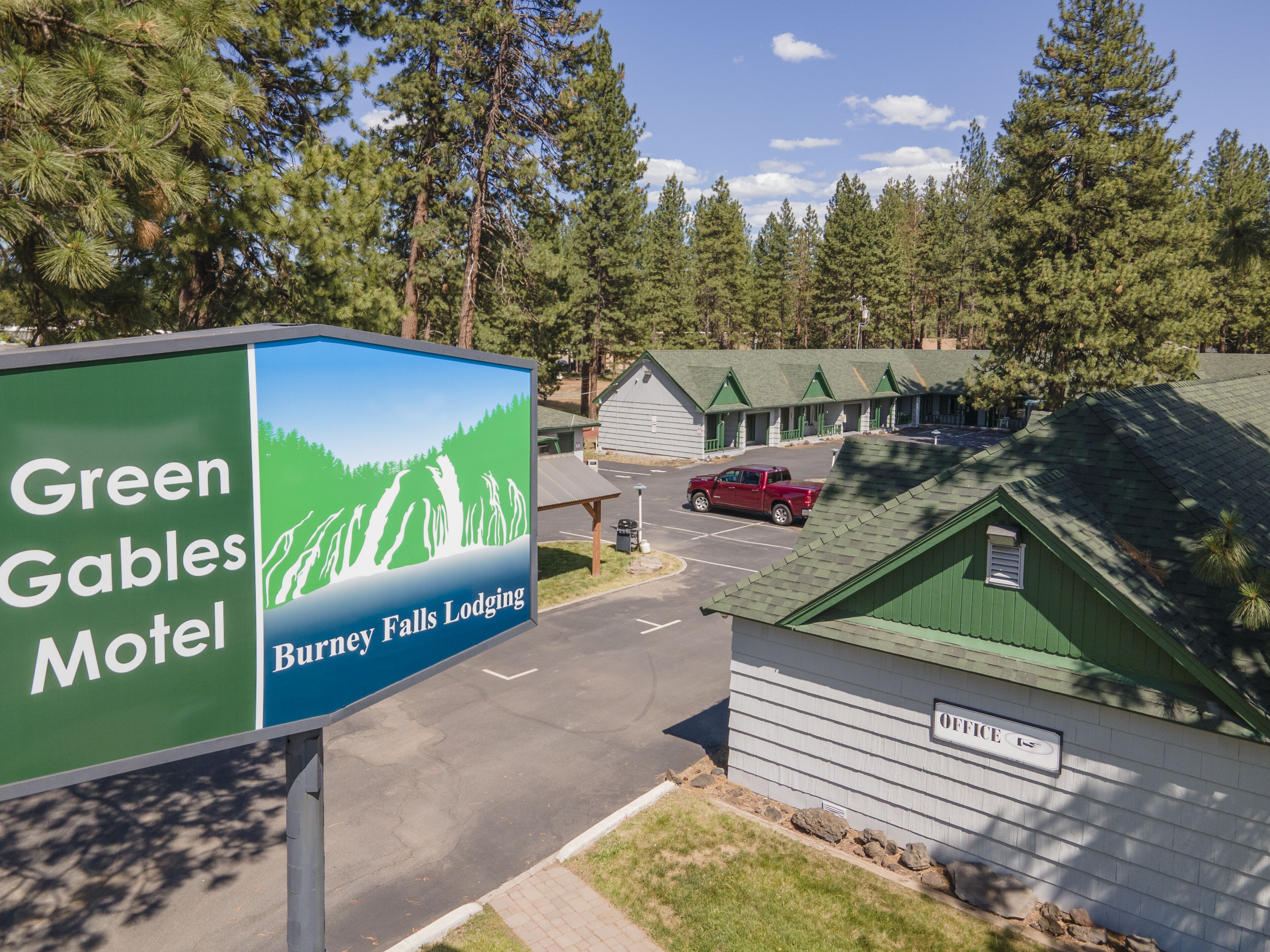 A motel sign with a mountain landscape, a parking lot, and a building with a green roof.