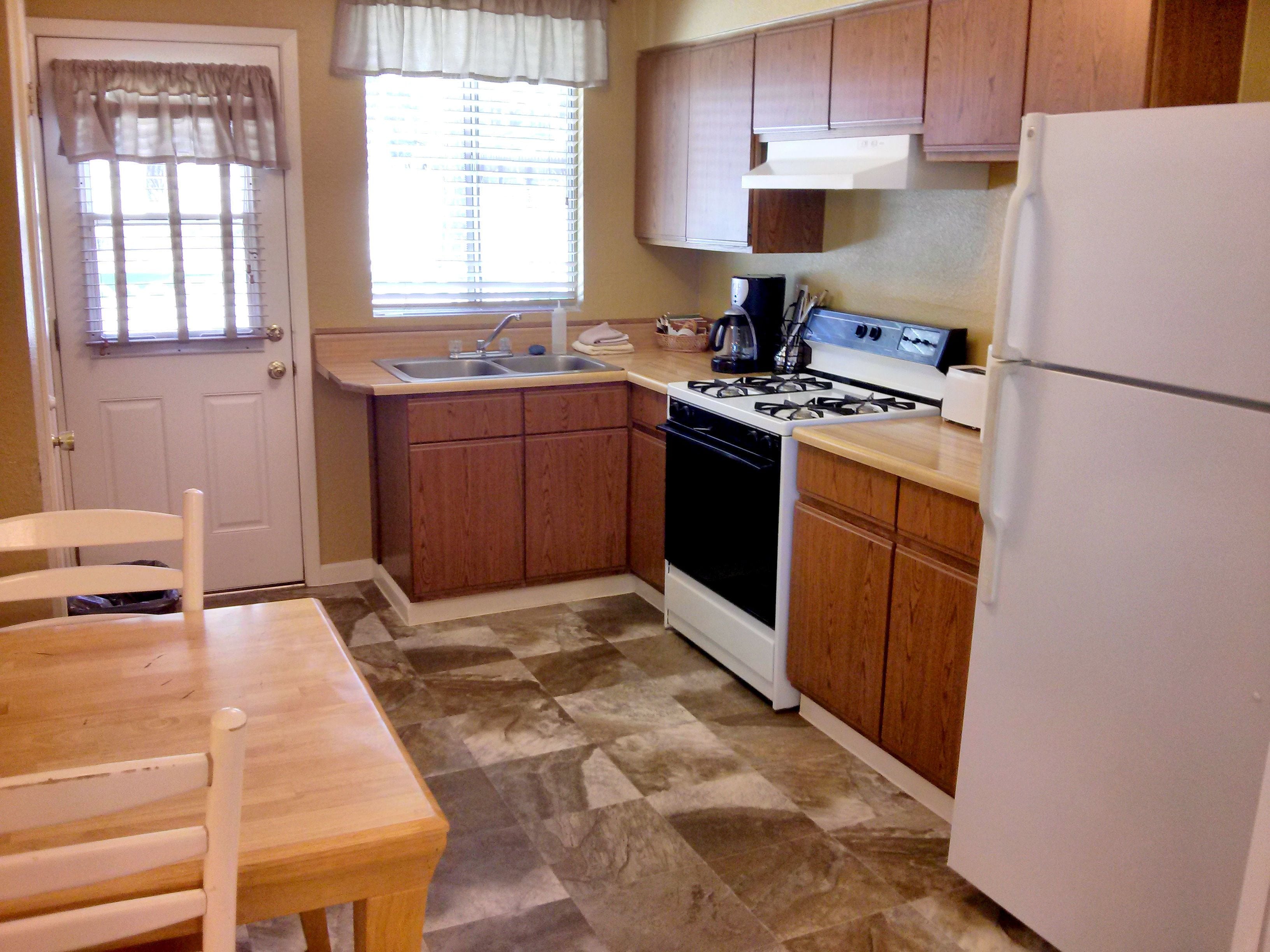 A compact kitchen with wooden cabinets, a white refrigerator, a stove, and a sink.