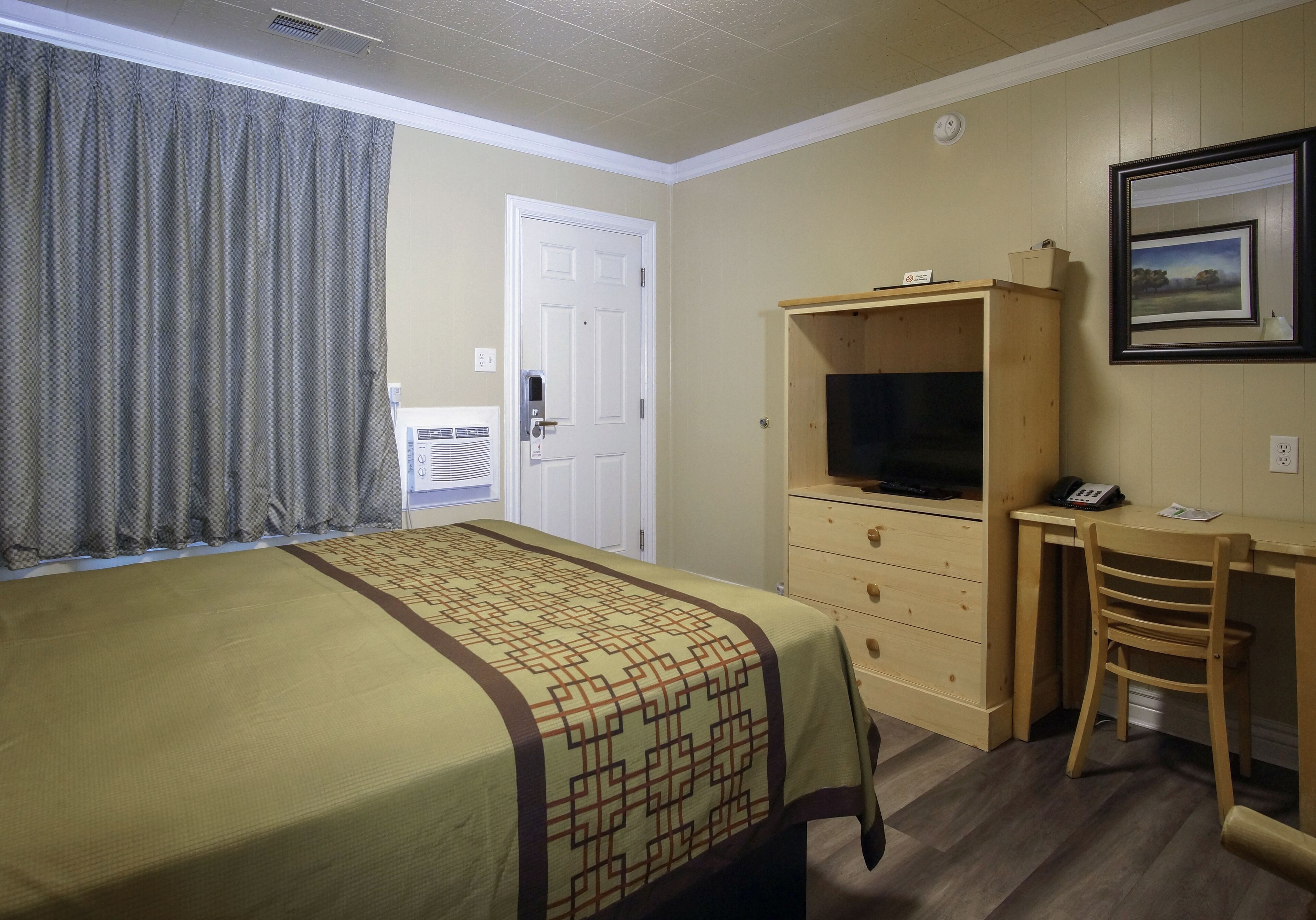 Una habitación de hotel con una cama, un escritorio con una silla, un televisor y una puerta.
