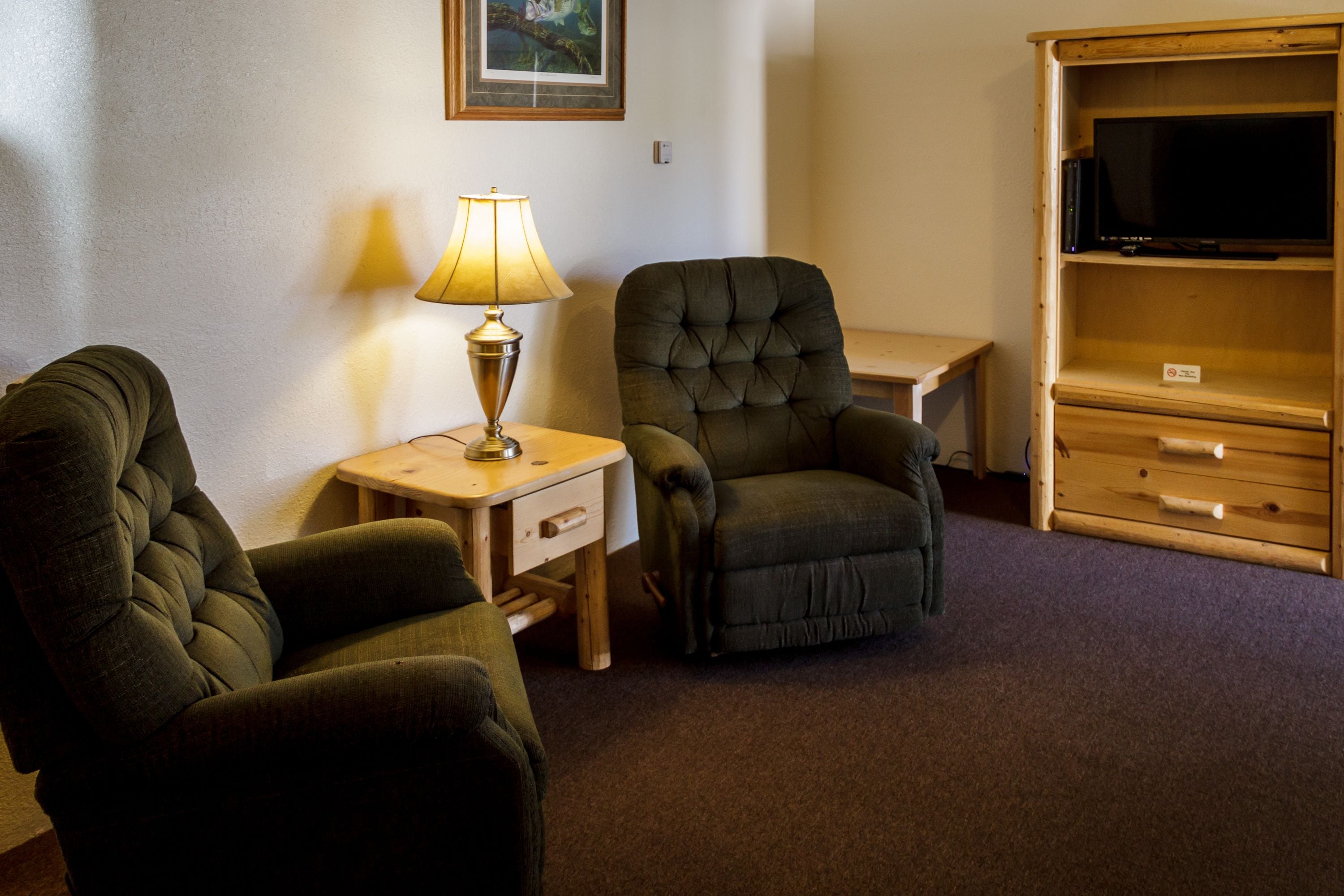 A room with two armchairs, a small table with a lamp, and a wooden cabinet with a television.