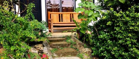 Un sendero de jardín que lleva a un banco de madera, rodeado de abundante vegetación y plantas en flor.