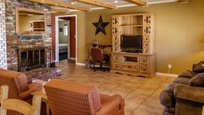 A spacious living area with a fireplace, wooden entertainment center, and comfortable seating. - Charm Motel & Suites (Burney)