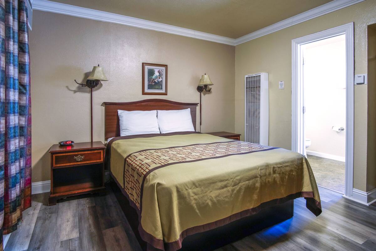 A hotel room with a bed, nightstands, lamps, a picture on the wall, and a door leading to a balcony.