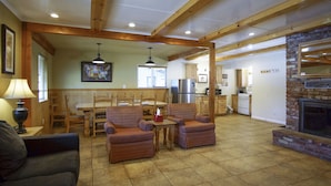 A spacious living room with a fireplace, wooden furniture, and a kitchen in the background. - Charm Motel & Suites (Burney)
