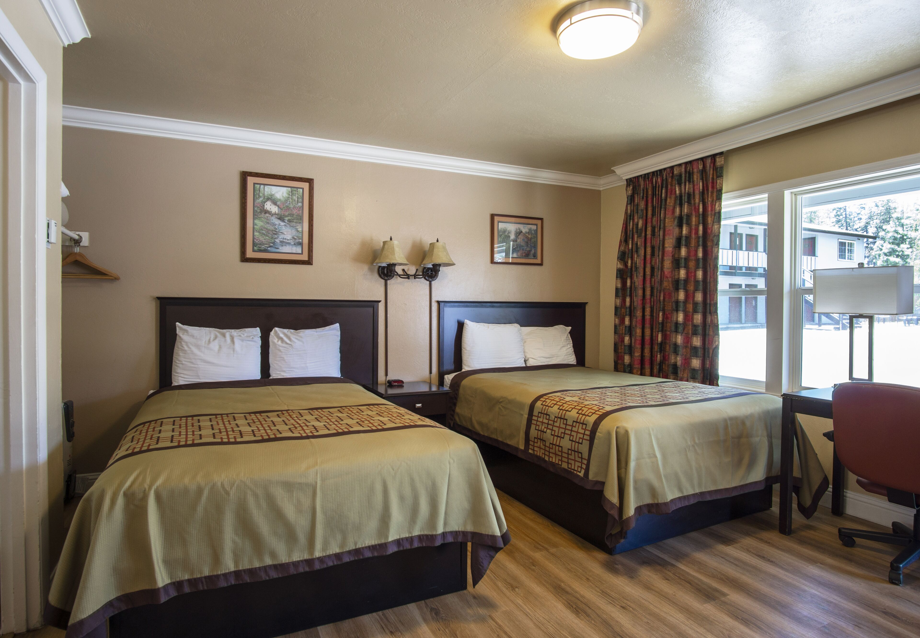 A hotel room with two beds, a desk, a chair, and a window with curtains.
