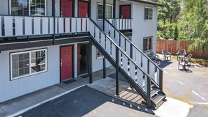 A two-story building with red doors, a staircase, and outdoor seating. - Charm Motel & Suites (Burney)