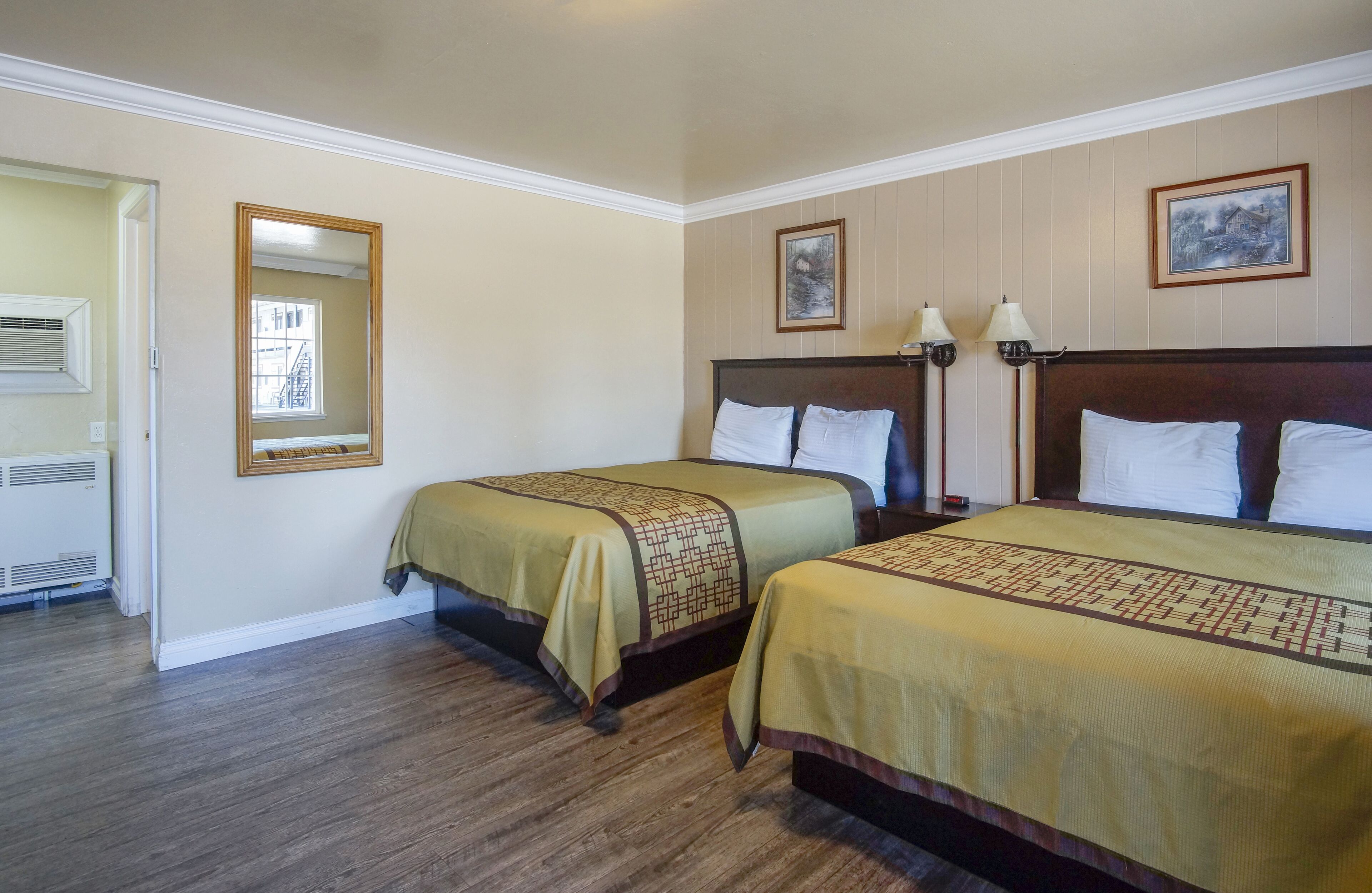 A hotel room with two beds, a large mirror, and two wall-mounted lamps.