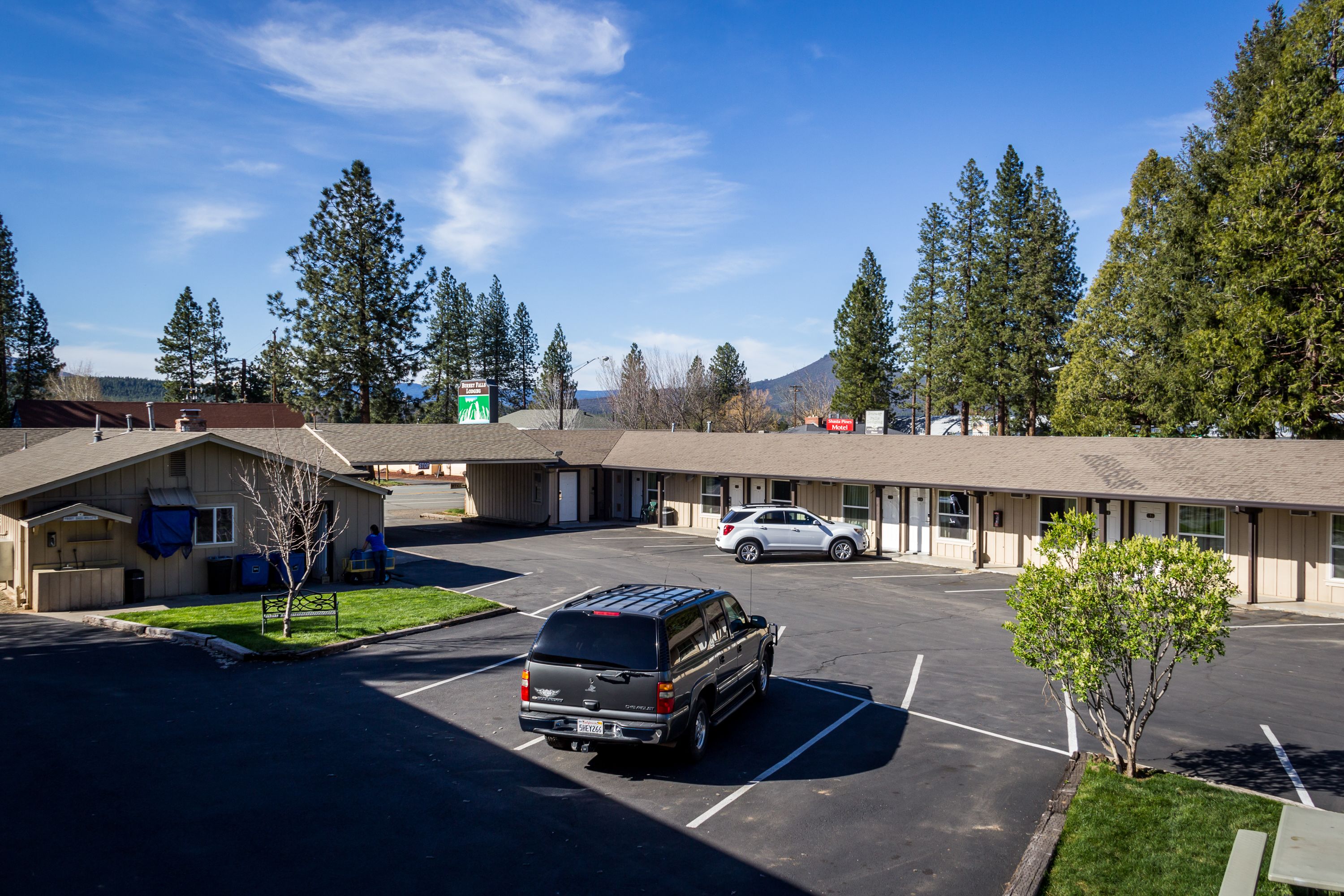 A motel with a parking lot, a small building with a covered area, and a mountain in the background.
