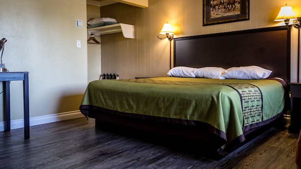 A hotel room with a large bed, a desk, a chair, and a wardrobe. - Charm Motel & Suites (Burney)