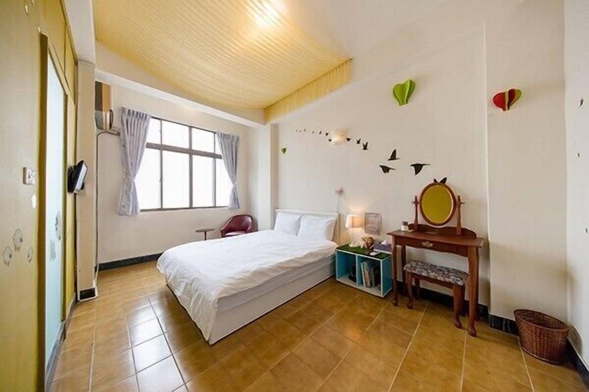 Quarto com cama, escrivaninha com espelho, cadeira e janela com cortinas.
