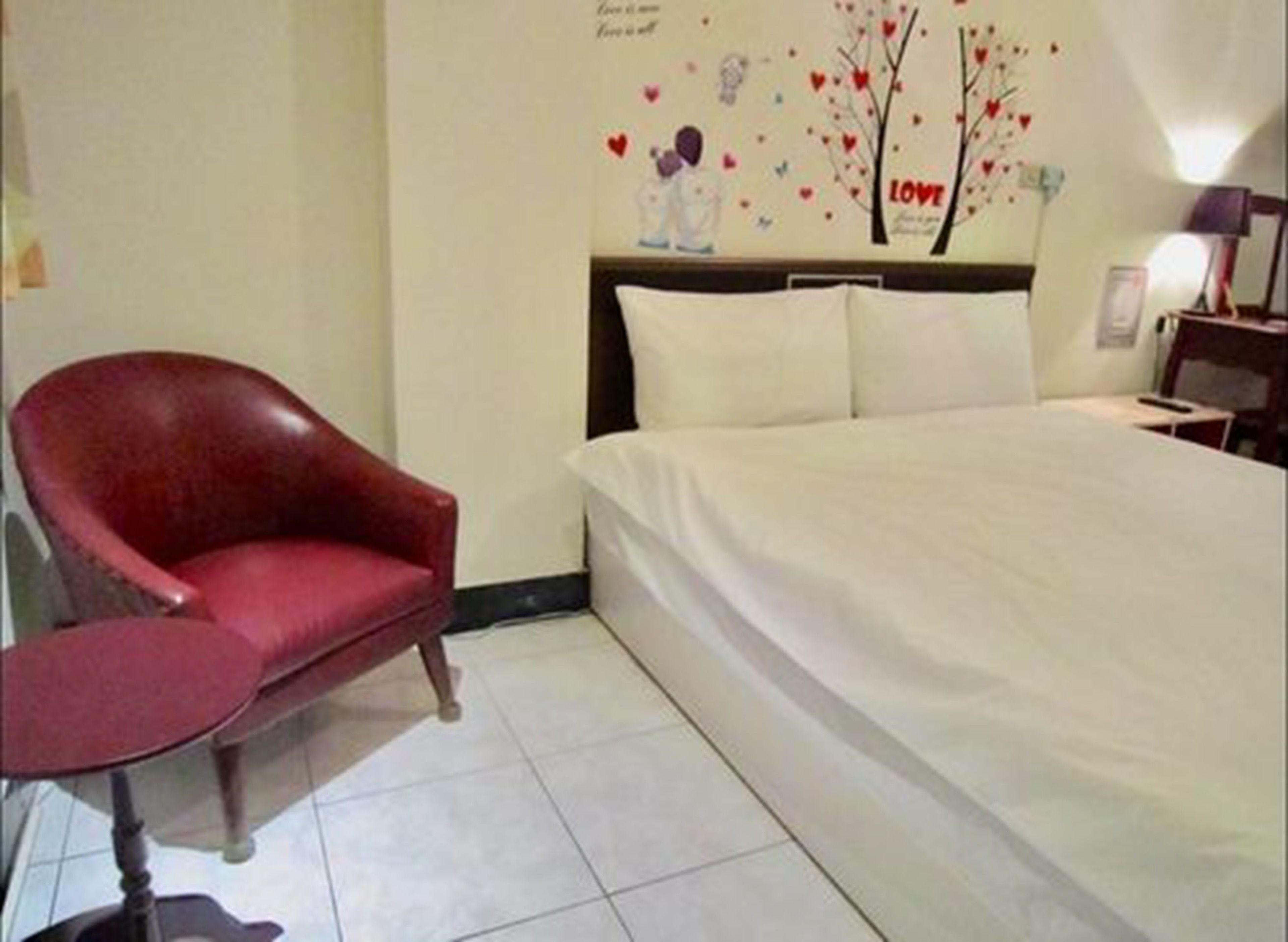A bedroom with a large bed, a red chair, and a wall decoration featuring hearts and a tree with the word "LOVE".
