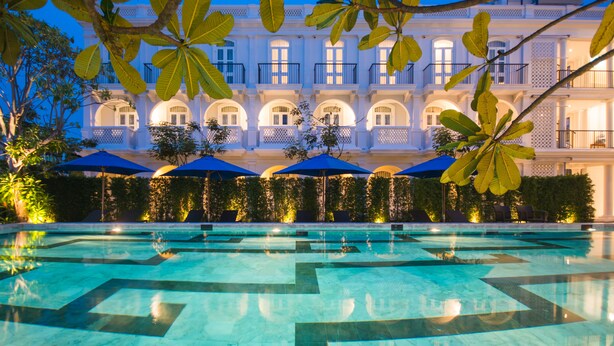 A pool area with a geometric tile pattern, surrounded by a white building with balconies and a hedge. - Little Nyonya Hotel (Wichit)