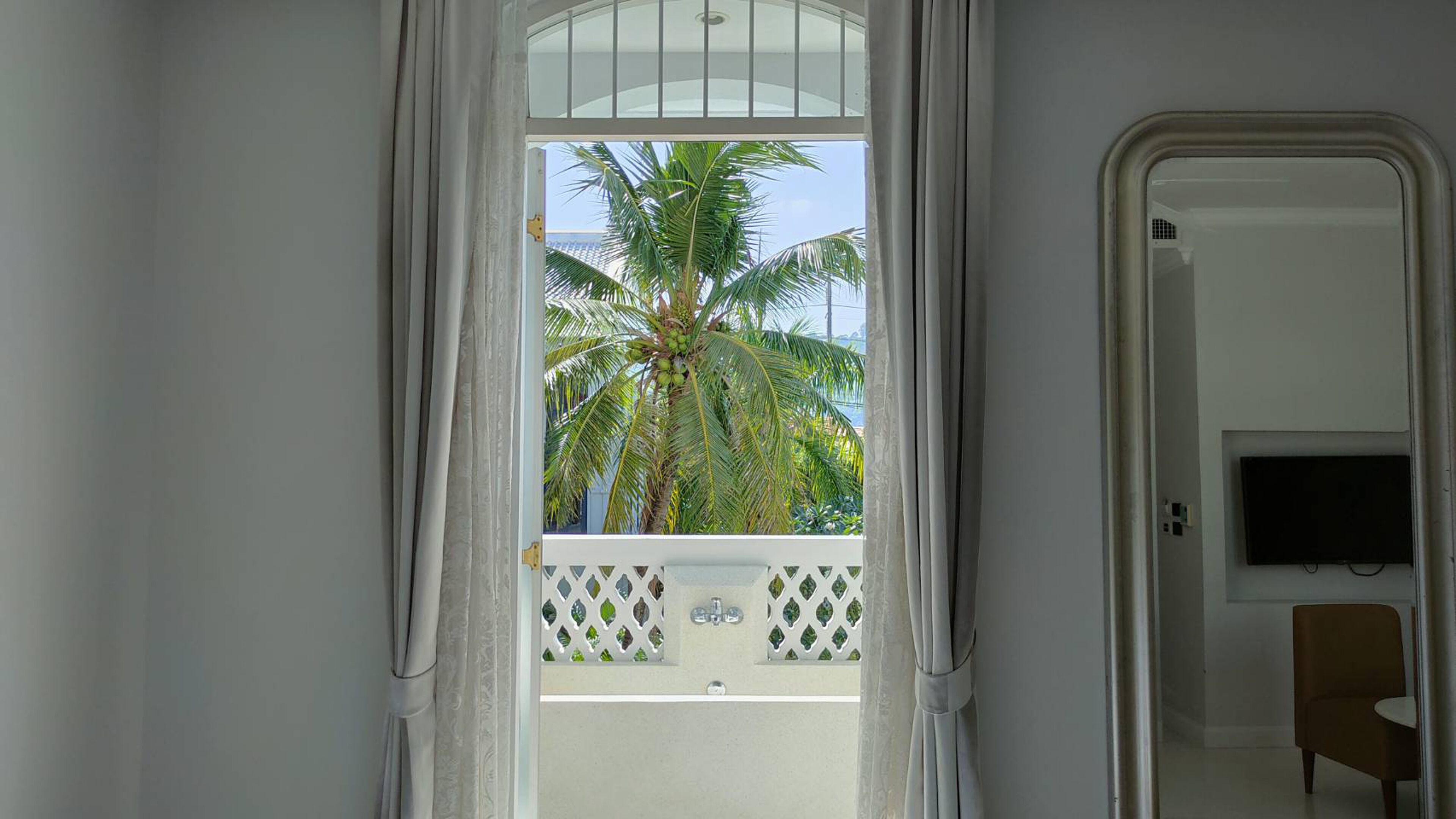 A room with a balcony, a TV mounted on the wall, and a chair.